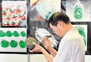 一名顾客在2014中国昆明泛亚石博览会上用手电筒仔细观看一块来自缅甸的翡翠原石。新华