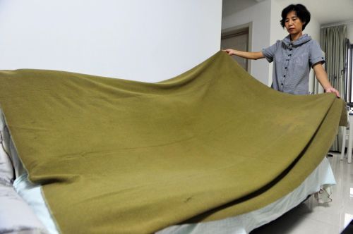 21日，李女士正在展示她父親保存下來的毛毯。 70多年過去了，這床軍綠色的毛毯保存良好。本報記者 王媛 攝