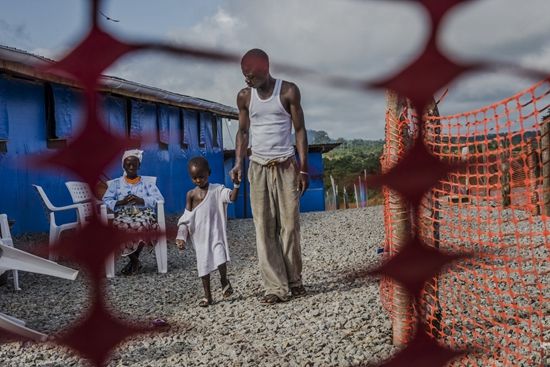 一名叫作George Beyan的埃博拉痊愈者和他埃博拉病毒检验呈阳性的5岁的儿子William一起在Bong County救护中心散步。医务人员告诉他，作为具有免疫能力的痊愈者，他是照料孩子的最佳人选。William在几天后死去。摄于2014年10月19日。 Daniel Berehulak 图