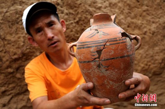 图为考古工作人员展示出土的仰韶文化时期代表性彩陶。中新社发 杨正华 摄