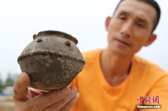 图为考古工作人员展示出土的带有腰带纹的仰韶文化时期的小黑陶罐。中新社发 杨正华 摄